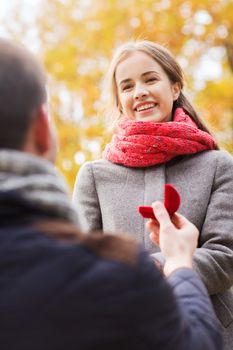 love, family, autumn and people concept - close up of smiling couple with engagement ring in small red gift box outdoors