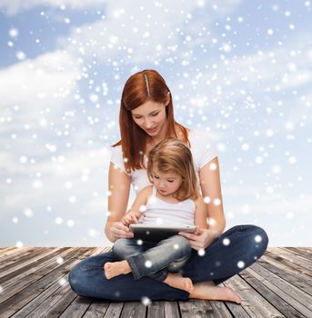 childhood, parenting, people and technology concept - happy mother with little girl and tablet pc computer over wooden floor and blue sky background