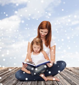 childhood, parenting, people and education concept - happy mother with little girl reading book over wooden floor and blue sky background