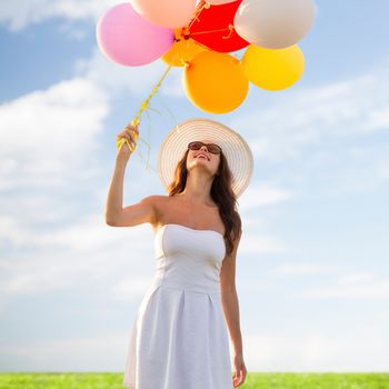 happiness, summer, holidays and people concept - smiling young woman wearing sunglasses with balloons over blue sky and grass background
