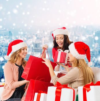 sale, winter holidays, christmas and people concept - smiling young women in santa helper hats with gifts and shopping bags over snowy city background
