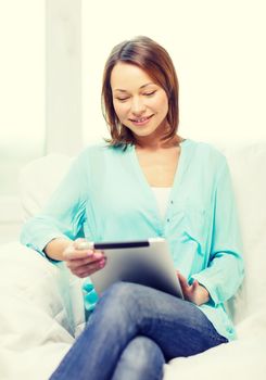 home, technology and internet concept - smiling woman sitting on the couch with tablet pc at home