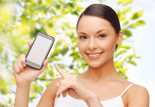 people, technology, communication and internet connection concept - happy young woman pointing finger to smartphone blank screen over green tree leaves background