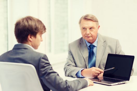 business, advertisement, technology and office concept - older man and young man with laptop computer in office