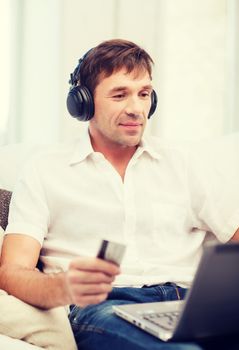 technology, leisure and lifestyle concept - happy man with headphones and credit card listening to music at home