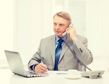 business, technologym communication and office concept - busy older businessman with laptop, charts, coffee and telephone in office