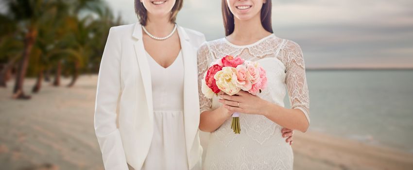 people, homosexuality, same-sex marriage, honeymoon and love concept - close up of happy married lesbian couple with flower bunch over tropical beach background