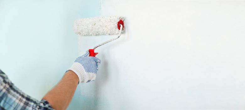 repair, building and home concept - close up of male in gloves painting wall with roller