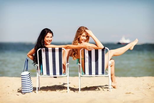 summer holidays and vacation - girls in bikinis sunbathing on the beach chairs
