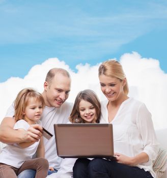 family, shopping, technology and people - happy family with laptop computer and credit card over blue sky and white cloud background