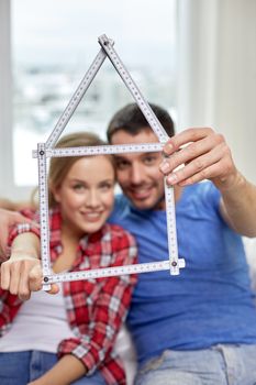 people, real estate and family concept - close up of happy couple looking through house shape made of ruler at home