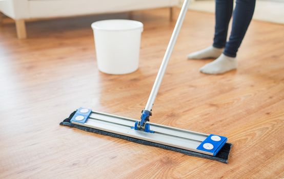 people, housework and housekeeping concept - close up of woman legs with mop cleaning floor at home