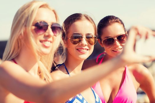 summer vacation, holidays, travel, technology and people concept- group of smiling young women on beach making selfie with smartphone over blue sky background