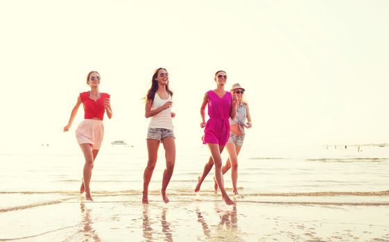 summer vacation, holidays, travel and people concept - group of smiling young women in sunglasses and casual clothes running on beach