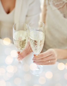 people, homosexuality, same-sex marriage, celebration and love concept - close up of happy married lesbian couple hands holding and clinking champagne glasses over holiday lights background