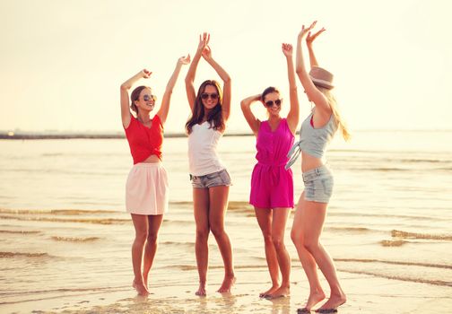 summer vacation, holidays, travel and people concept - group of smiling young women in sunglasses and casual clothes dancing on beach