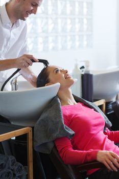 beauty and people concept - happy young woman with hairdresser washing head at hair salon