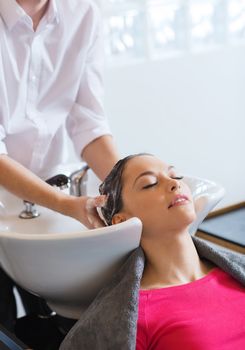 beauty and people concept - happy young woman with hairdresser washing head at hair salon