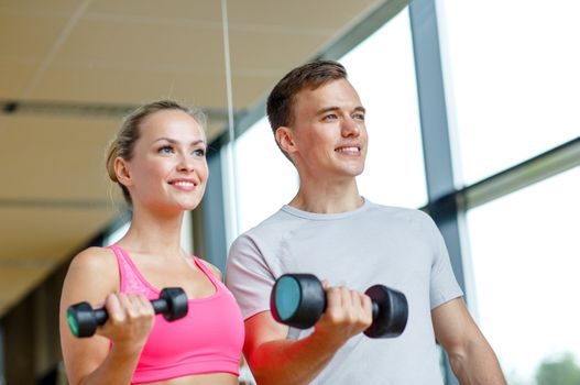 fitness, sport, exercising and diet concept - smiling young woman and personal trainer with dumbbells in gym