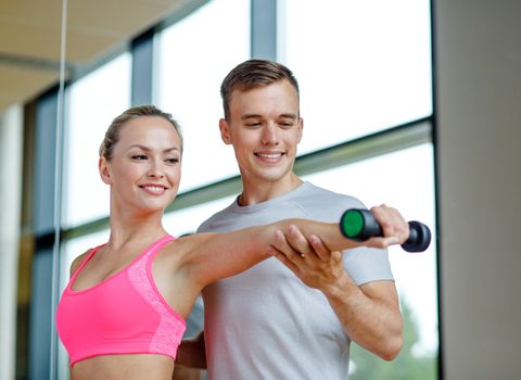 fitness, sport, exercising and diet concept - smiling young woman and personal trainer with dumbbell in gym