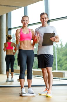 sport, fitness, lifestyle and people concept - smiling man and woman with scales and clipboard showing thumbs up in gym