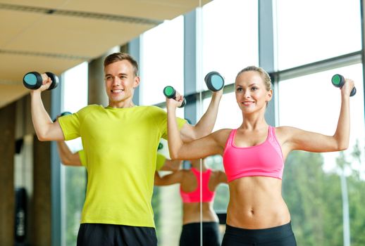 sport, fitness, lifestyle and people concept - smiling man and woman with dumbbells exercising in gym