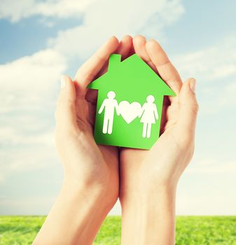 real estate and family home concept - closeup picture of female hands holding green paper house with family