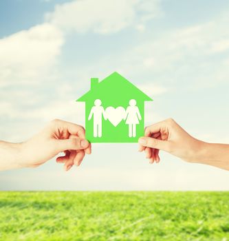 real estate and family home concept - isolated picture of male and female hands holding green paper house with family