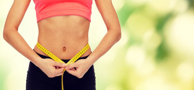 diet, sport, fitness and heath concept - close up of female hands measuring waist with measuring tape