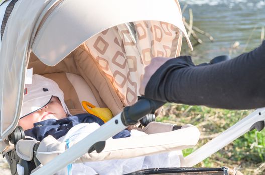 Sleeping little boy on a walk is in a stroller with a white cap.