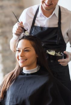 beauty and people concept - happy young woman with hairdresser coloring hair at salon