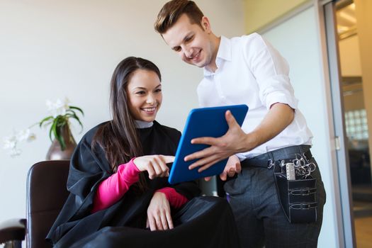 beauty, hairstyle, technology and people concept - happy young woman and stylist with tablet pc computer at salon