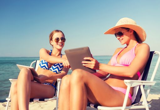 summer vacation, travel, technology and people concept - smiling women with tablet pc computers sunbathing in lounge on beach