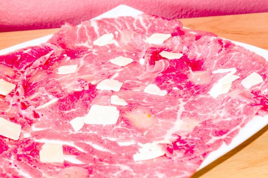 White dish with carpaccio of beef with parmesan.