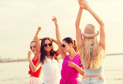 summer vacation, holidays, travel and people concept - group of smiling young women in sunglasses and casual clothes dancing on beach