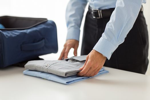 business, trip, luggage and people concept - close up of businessman packing clothes into travel bag