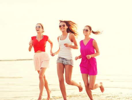 summer vacation, holidays, travel and people concept - group of smiling young women in sunglasses and casual clothes running on beach