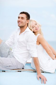 summer holidays and dating concept - couple in shades sitting at sea side