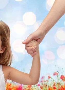 people, charity, family and adoption concept - close up of woman and little girl holding hands over blue lights and poppie field background