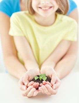 people, charity, family and ecology concept - close up of child and parent cupped hands holding soil with green sprout at home