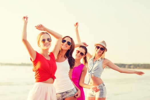 summer vacation, holidays, travel and people concept - group of smiling young women in sunglasses and casual clothes dancing on beach