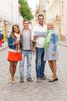 travel, vacation, technology and friendship concept - group of smiling friends with map and photocamera exploring city