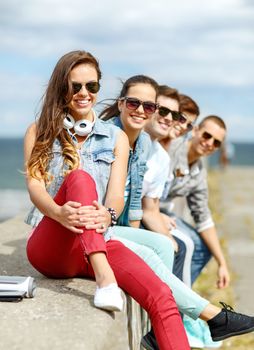 summer holidays and teenage concept - smiling teenage girl in sunglasses hanging out with friends outdoors