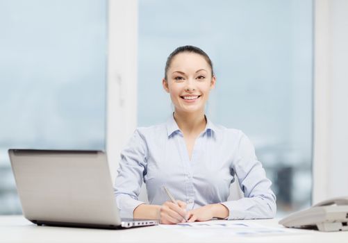 business, technology and communication concept - smiling businesswoman with phone, laptop and files in office