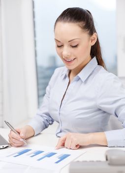 business, technology and communication concept - smiling businesswoman with phone, laptop and files in office