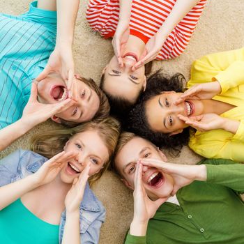 education and happiness concept - group of young smiling people lying down on floor in circle screaming and shouting