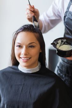 beauty and people concept - happy young woman with hairdresser coloring hair at salon