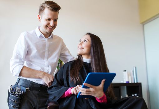 beauty, hairstyle, technology and people concept - happy young woman and stylist with tablet pc computer at salon