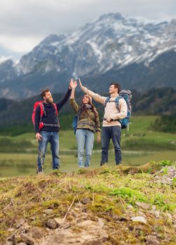 adventure, travel, tourism, hike and people concept - group of smiling friends with backpacks making high five gesture over mountains background