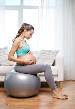 pregnancy, sport, fitness, people and healthy lifestyle concept - happy pregnant woman exercising on fitball at home